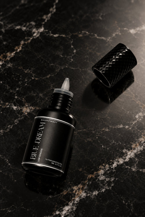 A small black bottle with a pointed applicator tip and a separate textured black cap, photographed on a plain light background. The bottle label reads 'BLUE DREAM'.